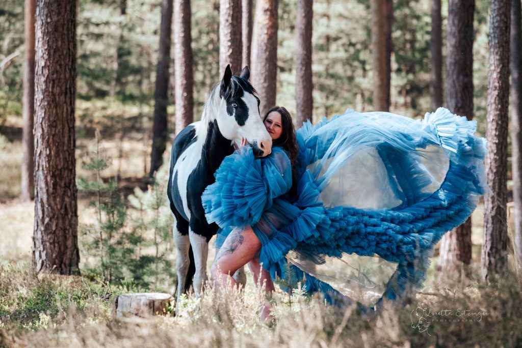 Eine Frau im blauen Kleid mit einem schwarz-weißen Pferd