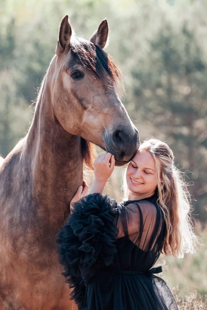 Eine Frau in einem schwarzen Kleid steht bei einem braunen Pferd