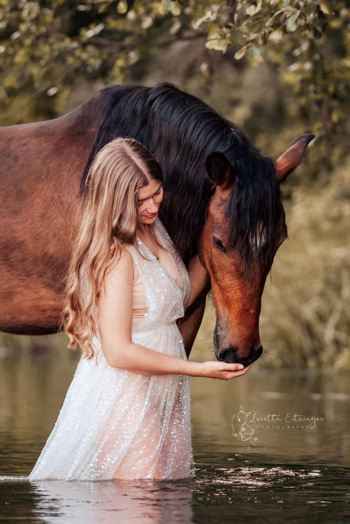 Eine Frau steht im Wasser und ein braunes Pferd steht daneben.