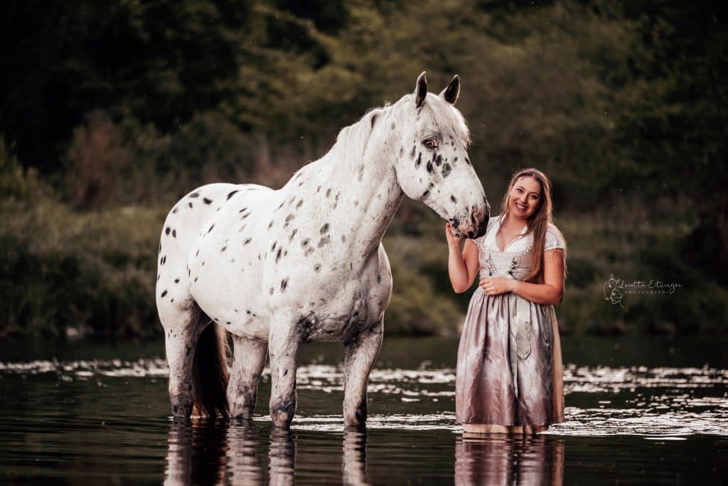 Eine Frau steht im Dirdl mit ihrem Pferd im Wasser