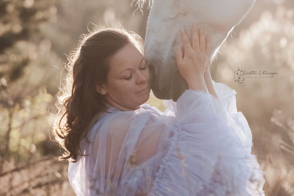 Eine Frau im weißen Kleid hält ihren Kopf an die Nase des Pferdes
