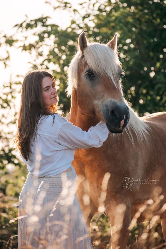 Eine Frau im weißen Kleid steht neben einem braunen Pferd.